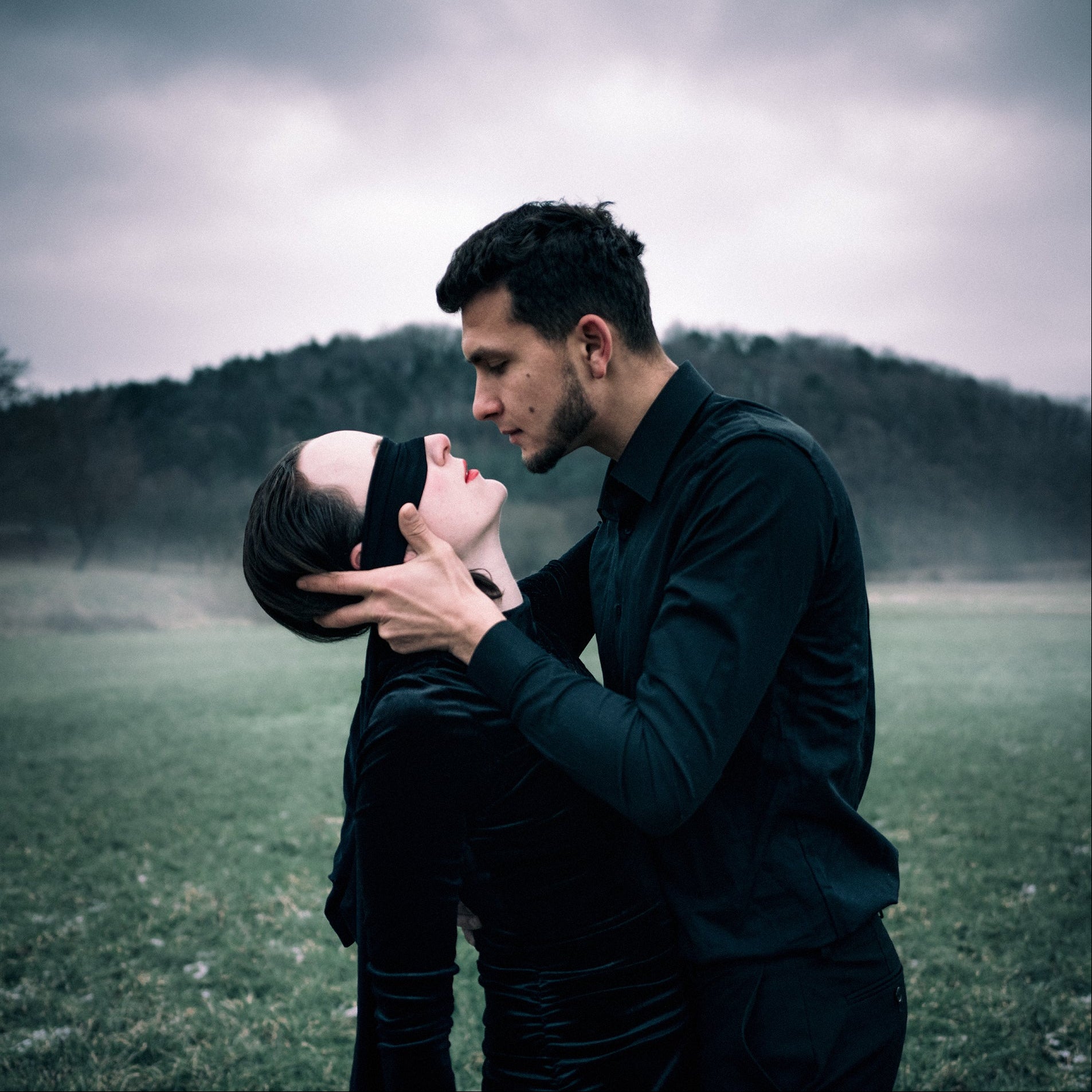 Two people embracing in a field with a cloudy sky