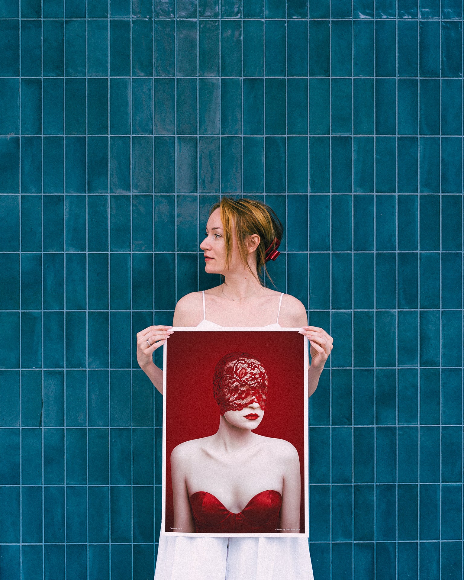 Woman holding a framed artwork against a blue tiled wall