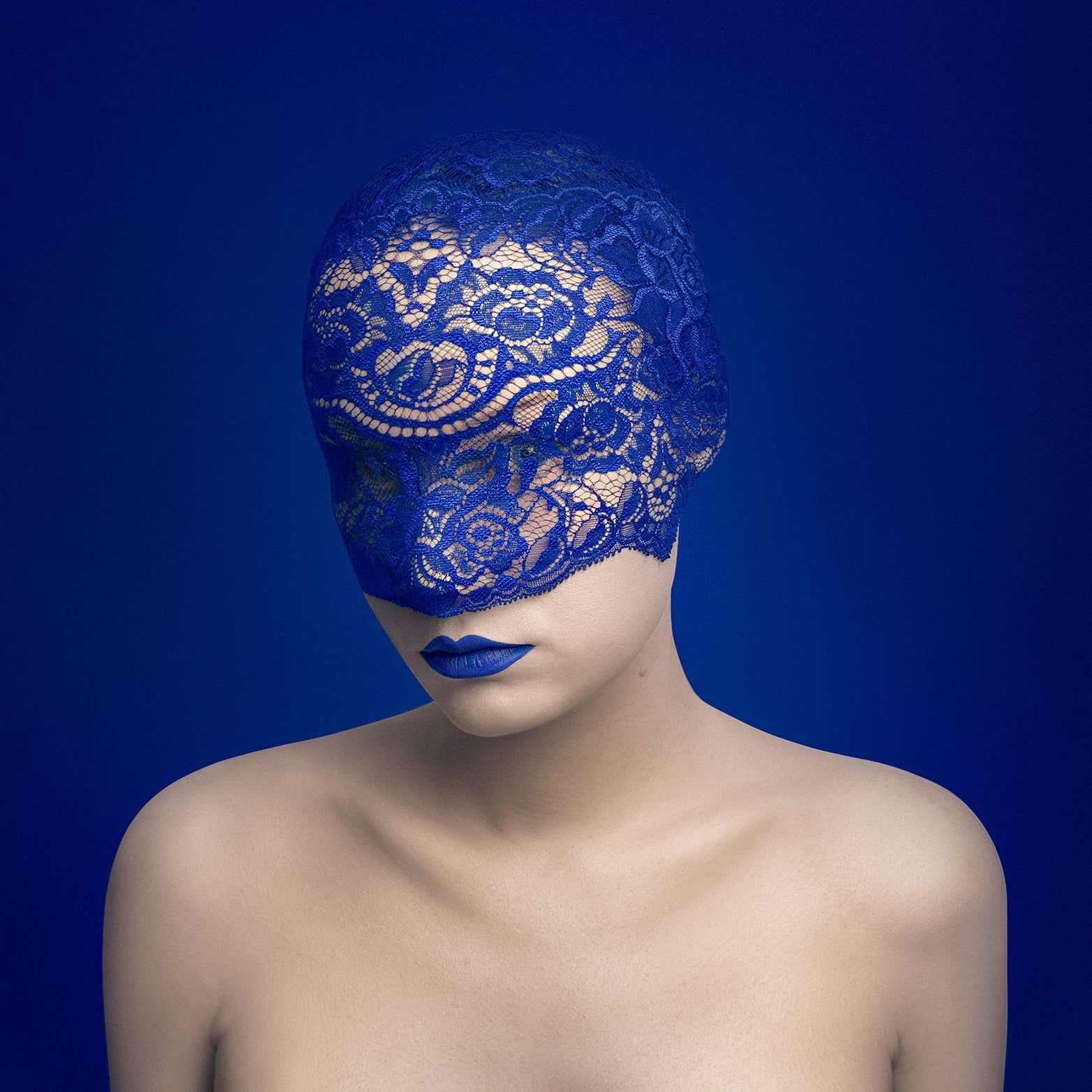 Woman wearing a blue lace mask and lipstick against a dark blue background
