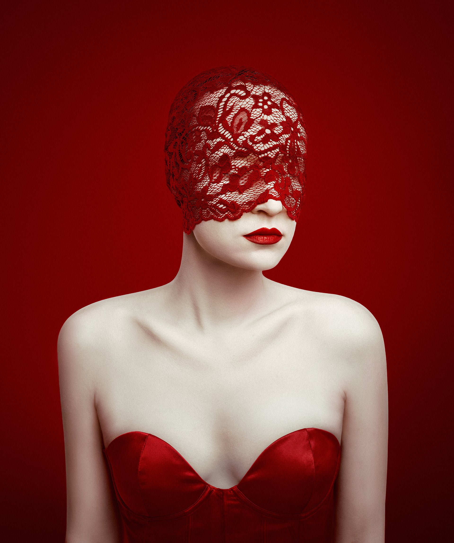 Woman wearing a red lace head covering and red dress against a red background