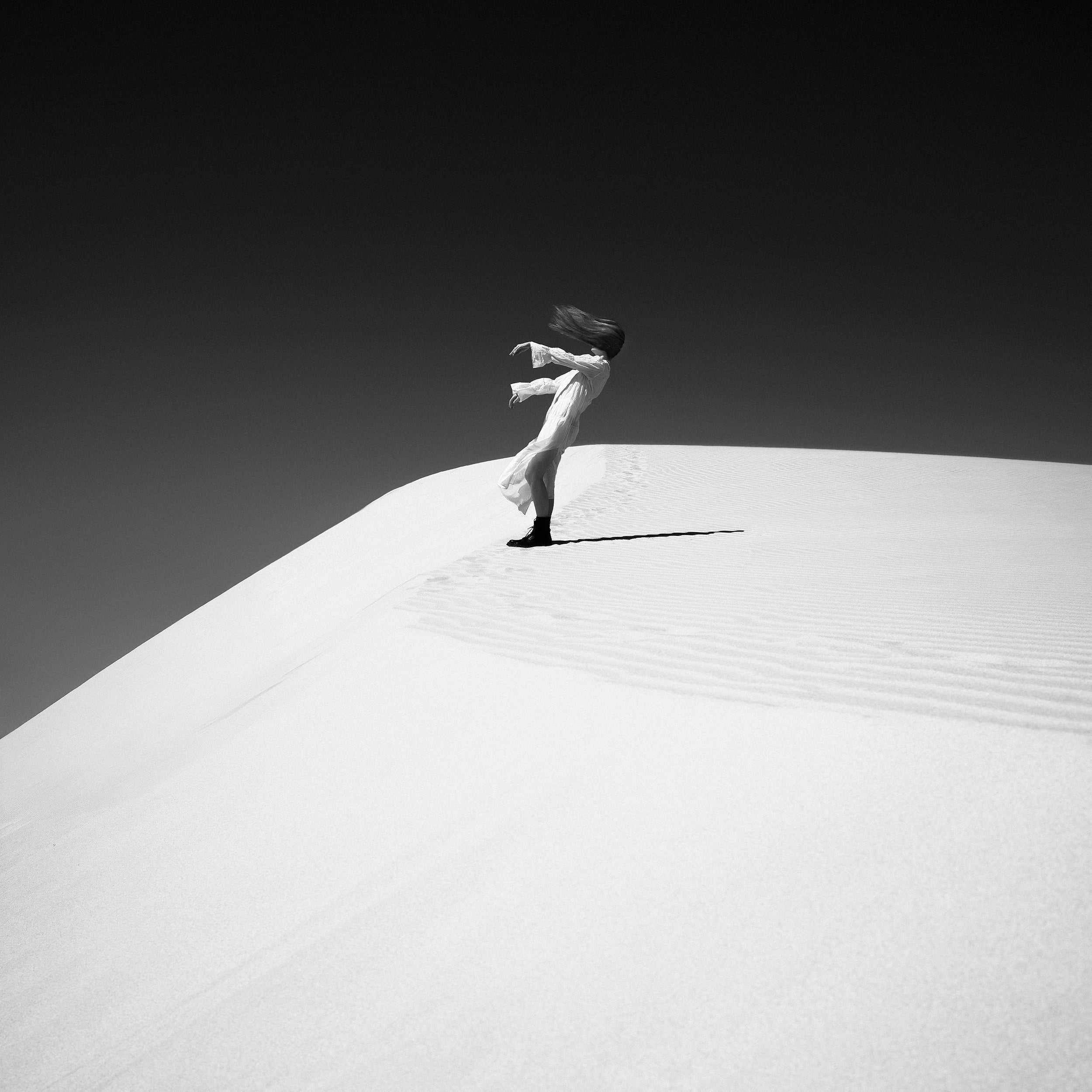 Person sitting on a sand dune with a minimalistic black and white color scheme