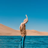 Person standing by a body of water with sand dunes and clear blue sky in the background