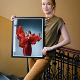 Woman holding a framed photograph of a woman in a red dress on a staircase.