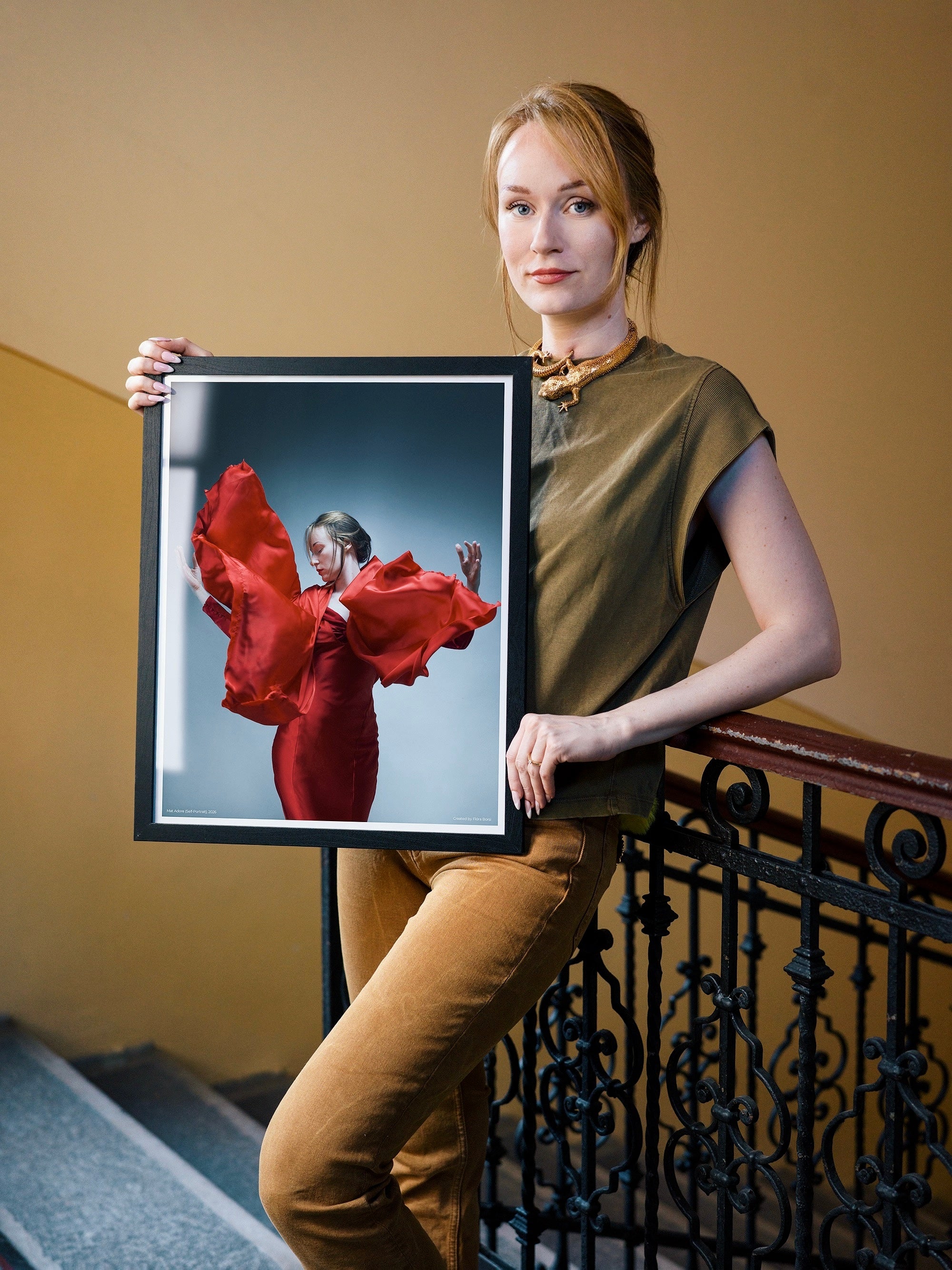 Woman holding a framed photograph of a woman in a red dress on a staircase.