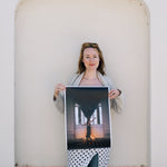 Woman holding a large photograph against a light-colored wall.