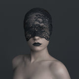 Person wearing a black lace mask and dress against a dark background