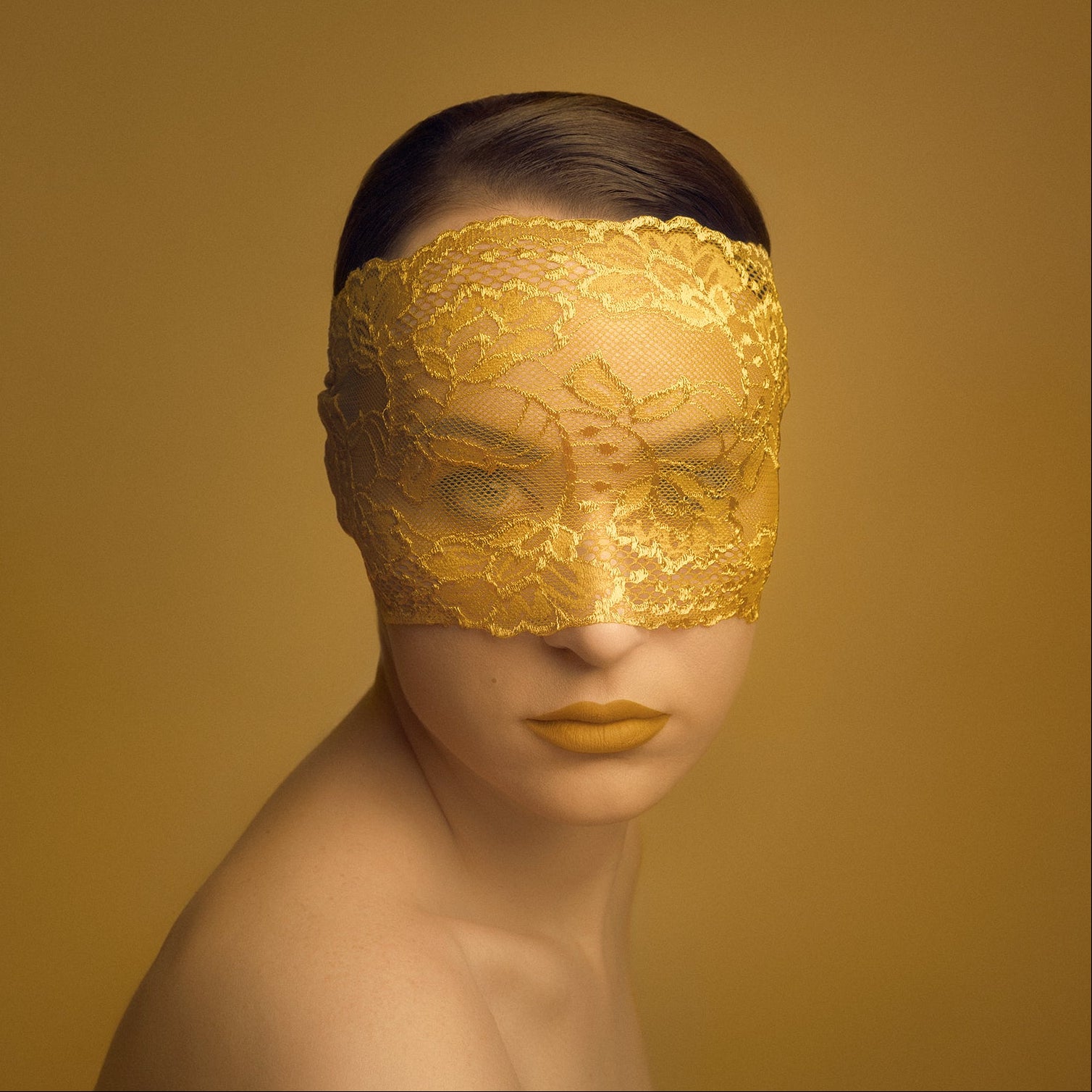 Person wearing a gold lace eye mask against a yellow background