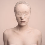 Woman wearing a lace blindfold against a soft pink background