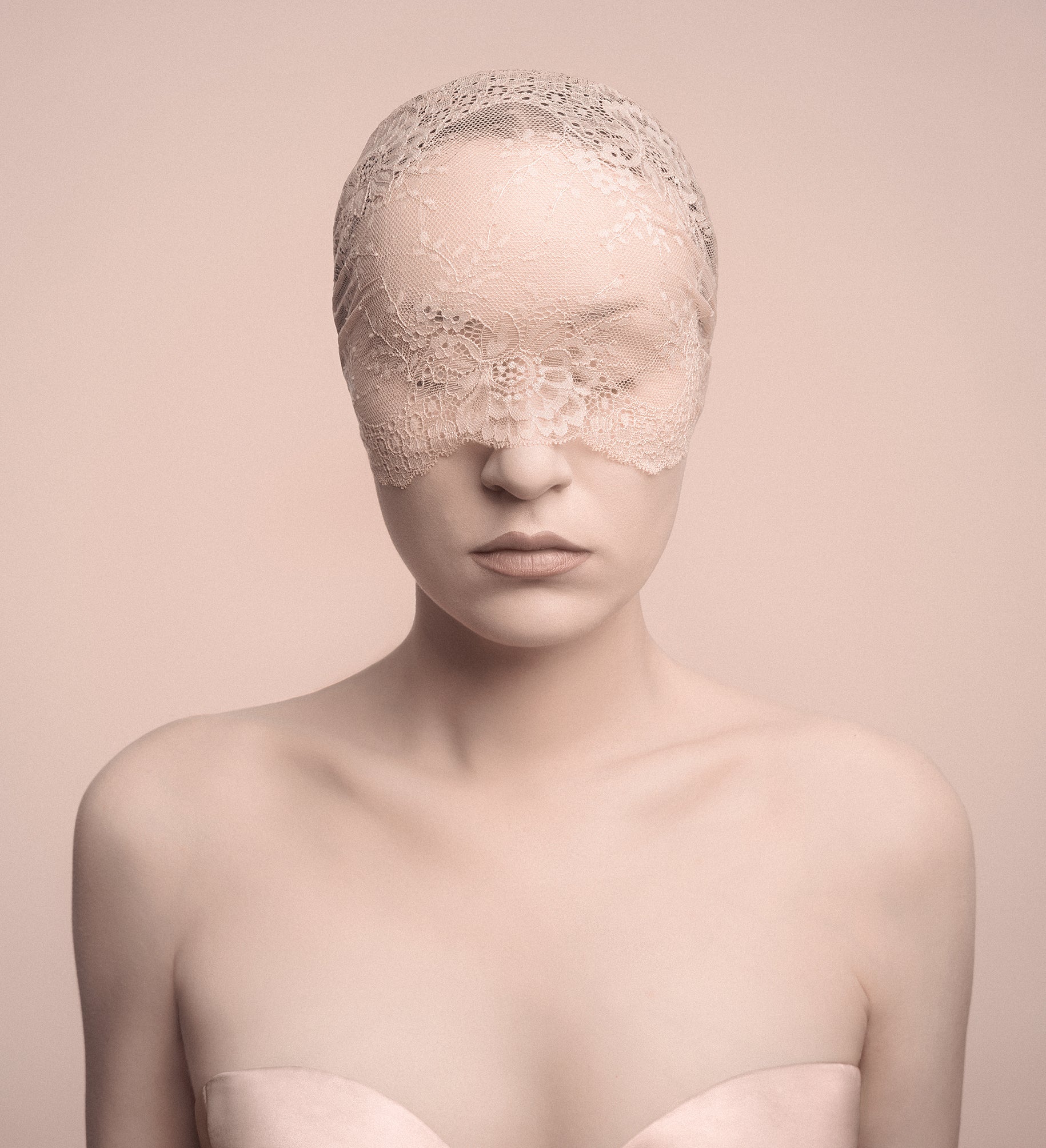 Woman wearing a lace blindfold against a soft pink background