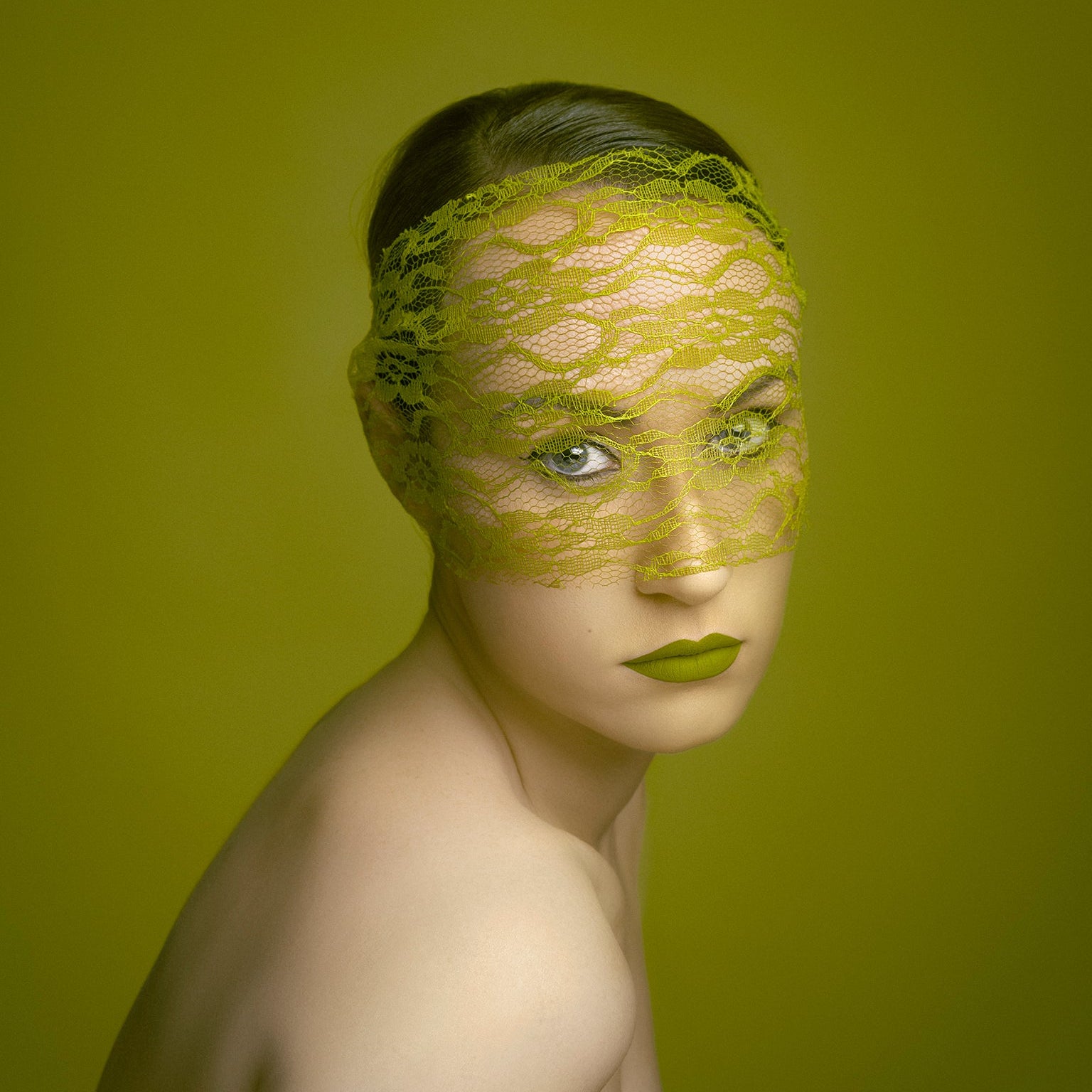 Woman wearing a green lace mask against a matching green background